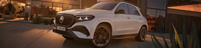 Weißer Mercedes-Benz GLE 2026 vor modernem Haus bei Sonnenuntergang mit markantem Kühlergrill und schwarzen Felgen