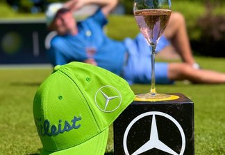 ein grünes Basecap und ein Glas Sekt auf einem Würfel mit Mercedes-Benz Logo