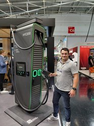 Mann steht an einer großen, schwarzen Ladesäule mit grünem Rand und der Aufschrift 'HYC200' auf der Messe Intersolar