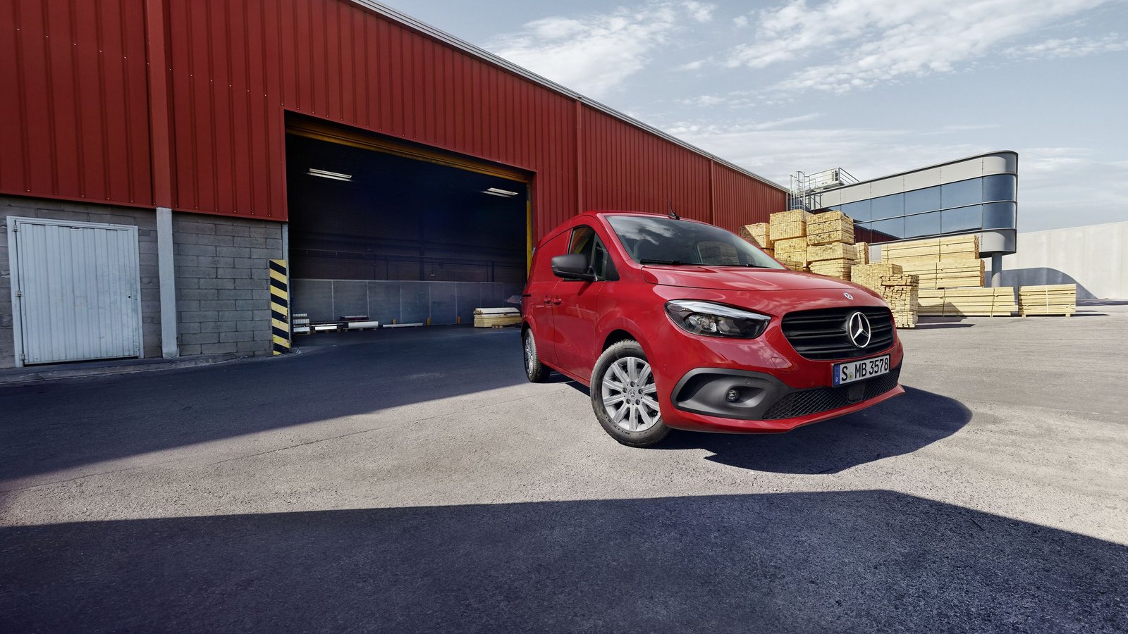 Mercedes-Benz Citan Kastenwagen in Rot, Frontansicht vor einem großen roten Lagergebäude mit gestapelten Holzpaletten im Hintergrund.