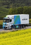 Mercedes-Benz eActros 400 Elektro-Lkw fährt auf Landstraße vorbei an gelb blühendem Feld und bewaldeten Hügeln im Hintergrund