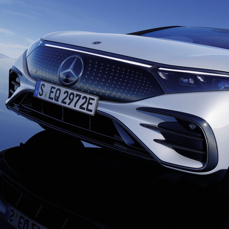 Frontansicht des Mercedes-Benz EQS mit Stern Kühlergrill-Design vor reflektierend blauem Hintergrund.