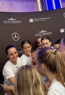 Gruppe von jungen Menschen in weißen T-Shirts steht im Kreis und legt die Hände zusammen vor eine schwarze Werbewand mit Mercedes-Sternen und den Logos von Schloss Wöllenstein und Kraftverkehr