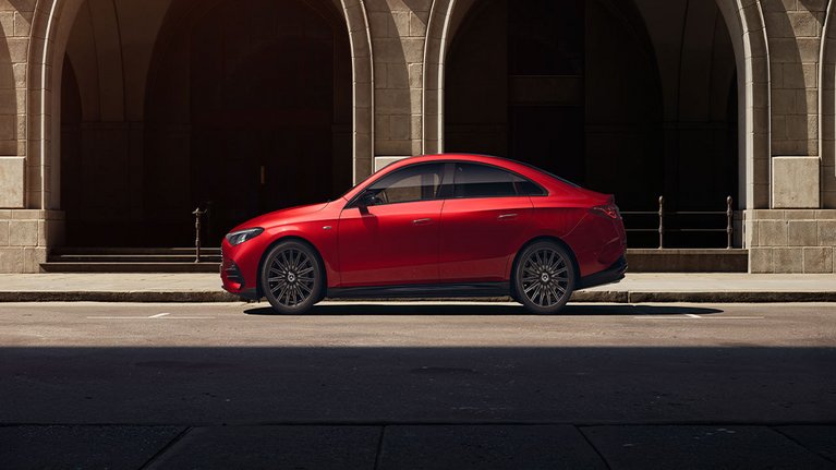 Mercedes-Benz CLA 250+ in Rot von der Seite vor historischer Fassade – fließende Linien und coupéhaftes Design.