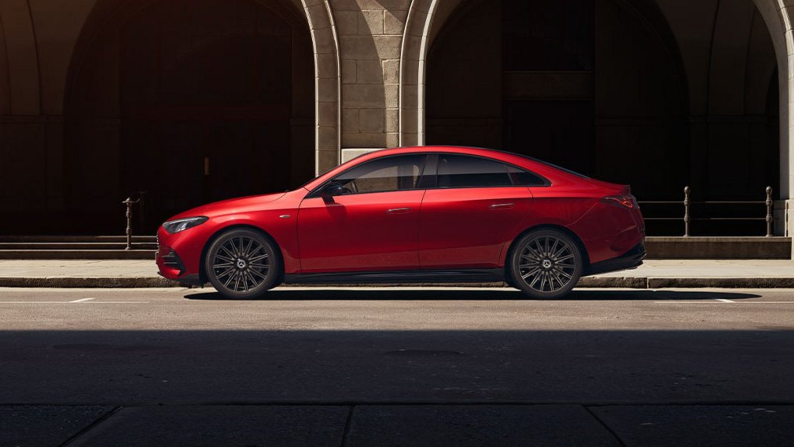 Mercedes-Benz CLA 250+ in Rot von der Seite vor historischer Fassade – fließende Linien und coupéhaftes Design.