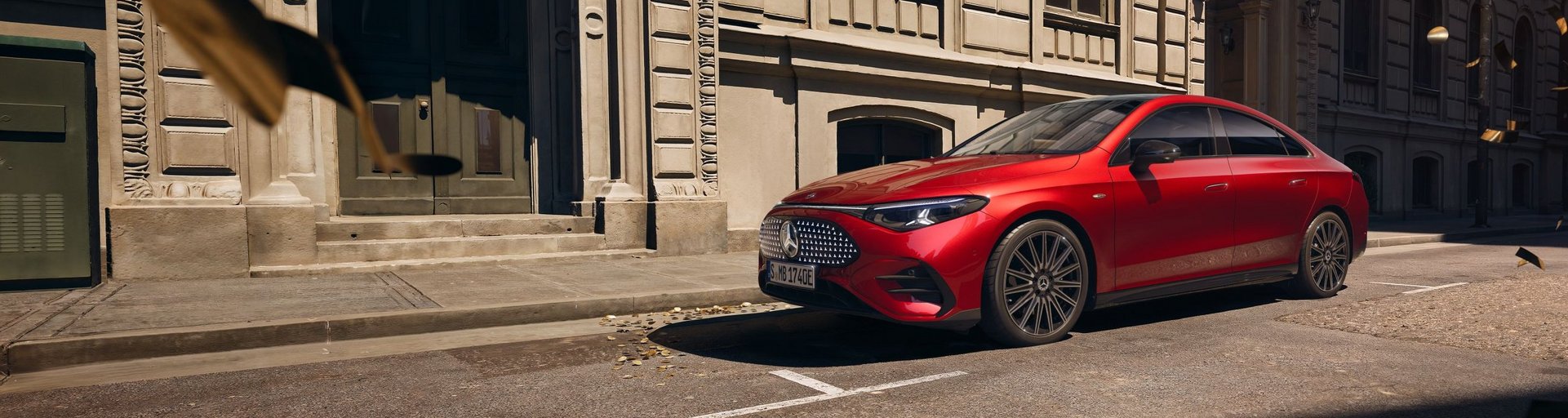 Neuer Mercedes-Benz CLA 250+ in Rot seitlich aufgenommen vor historischer Stadtkulisse mit modernen Designelementen.